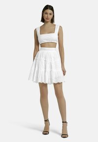 Weißes Zwei-Teiler-Outfit mit einem kurzen Oberteil mit quadratischem Ausschnitt und einem gestuften Rock, beide mit bestickten Details und geschnittenen Kanten.