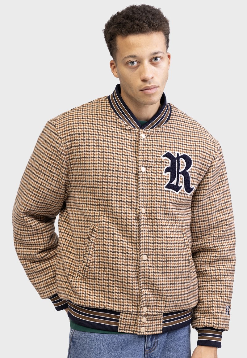Veste à motif pied-de-poule tan avec col et poignets côtelés navy, fermeture à bouton et un grand logo "R" navy sur la poitrine.