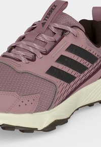 Chaussure de trail running Adidas Terrex mauve avec tige en mesh, bandes noires, lacets à motif, col rembourré et semelle blanche texturée.