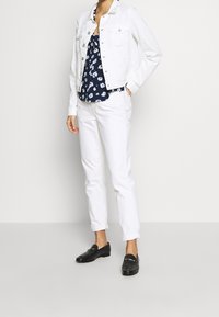 Chaqueta de mezclilla blanca y pantalones combinados con una blusa navy de estampado floral. Mocasines negros completan el conjunto. Enfóquese en las líneas limpias y los colores contrastantes.