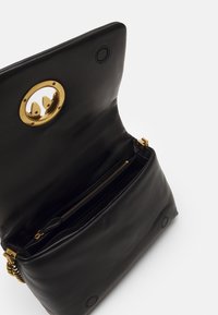 Borsa in pelle nera con un accento di hardware dorato arrotondato e scomparto con zip. Texture liscia e design semplice. Vista interna mostrata.