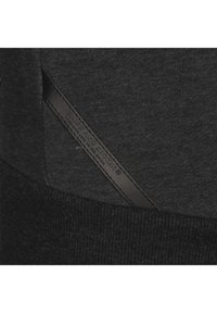 Sudadera negra con tejido texturizado, dobladillo acanalado y una etiqueta de cuero con marca en relieve integrada en la costura lateral.