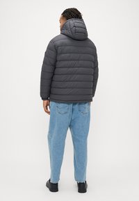 Γκρι μπουφάν με κουκούλα, με οριζόντια υφασμένη υφή και ελαστικές μανσέτες, συνδυασμένο με χαλαρά ανοιχτό μπλε τζιν και μαύρα παπούτσια.