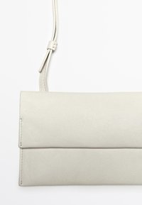 Borsa a tracolla in pelle grigia chiara con design piatto, lunga tracolla regolabile e una finitura leggermente texturizzata. Presenta una semplice patta pieghevole.