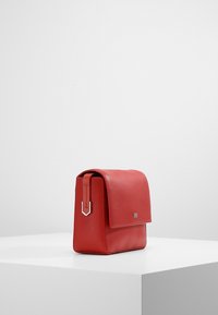 Rød lædertaske med en tekstureret overflade, rektangulær form, en klaplukning og en detalje i sølvfarvet metal på remmen.