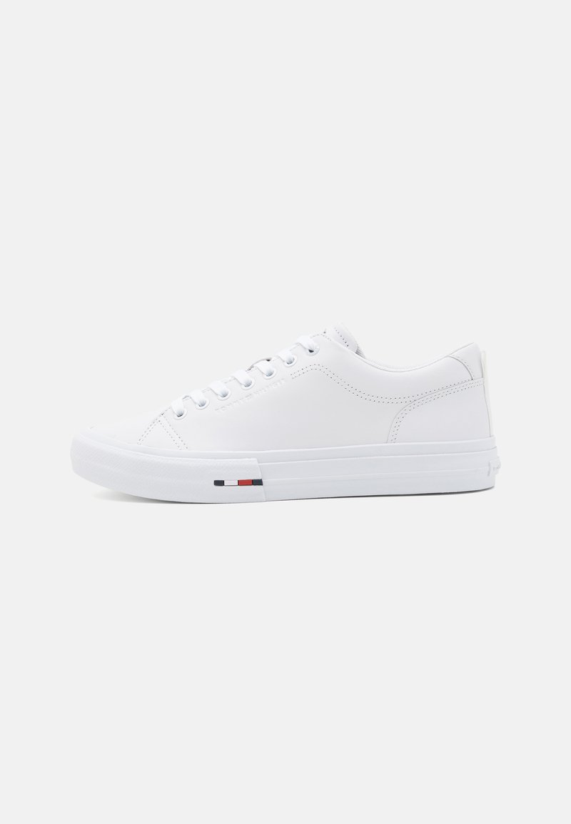 White sneaker made of smooth leather with a rounded toe, metal eyelets, and a tri-color accent near the sole. Textured rubber sole.