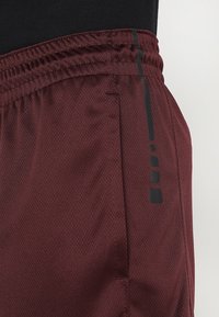 Bordeauxrote Sportshorts aus texturiertem Netzstoff, mit elastischem Taillenbund, Seitentasche und einem schwarzen vertikalen Akzentdesign.