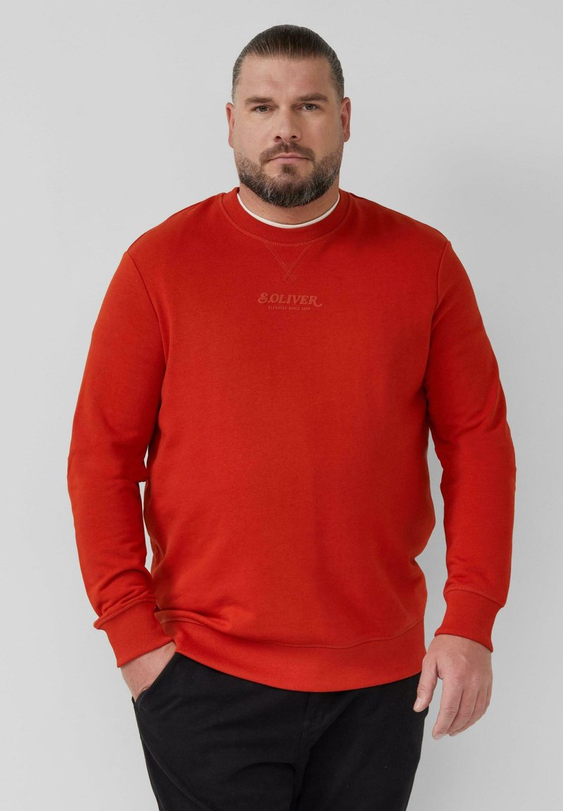 Punane pusle pikkade varrukatega ja ümara kaelaauguga. Rinnal on diskreetne logo. Pehme kangas sileda tekstuuriga.