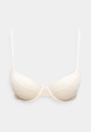 Soutien-gorge rembourré couleur crème avec bretelles fines réglables et détails en dentelle sur les bonnets et les côtés, présenté sur un fond uni.