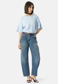 Šviesiai mėlynas per didelis marškinėliai derinami su laisvo kirpimo, išblukusiais mėlynais džinsais, turinčiais dvi priekinės kišenes ir rudą odinį diržą.