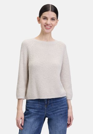 Light beige knit sweater with a textured pattern, round neckline, and three-quarter sleeves, paired with blue denim jeans.