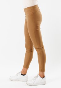 Leggings beige con un design aderente, dotati di una vita alta, texture liscia e orlo alla caviglia, abbinati a sneakers bianche.