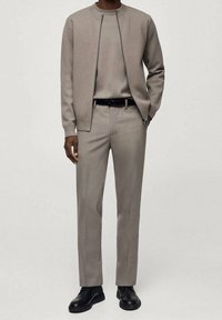 Beige knit cardigan, matching sweater, and tailored trousers. Black belt and shoes. Smooth texture, minimalistic design, slim fit.