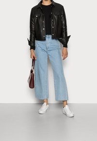 Osoba v černé kožené bundě, černém topu, světlých modrých širokých džínách, bílých teniskách, držící tmavě červenou kabelku.