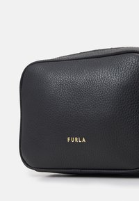 Černá kožená taška s texturovaným povrchem, na přední straně se zlatým logem "FURLA", obdélníkový tvar s zaoblenými hranami.