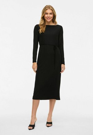 Black long-sleeve dress with a textured pattern, fitted waist tie, and a midi length. Features a boat neckline and straight silhouette.