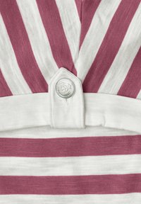 Nahaufnahme eines bordeauxroten und weißen gestreiften Stoffs mit einer weißen Lasche, die durch einen silbernen Knopf mit detailliertem Emblem befestigt ist.