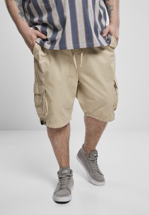 Beige cargoshorts met zijzakken, een trekkoord tailleband en gestikte zomen, gecombineerd met grijze sneakers. Gestreepte shirt is gedeeltelijk zichtbaar.