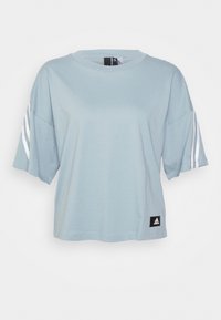 Světle modré zkrácené tričko Adidas s bílými třemi pruhy na rukávech a černou nášivkou loga Adidas na spodním okraji.
