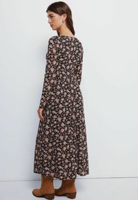 Sort blomster midi kjole med lange ærmer, prydet med pink-orange blomster og en afslappet pasform. Sammen med brune ankelstøvler.
