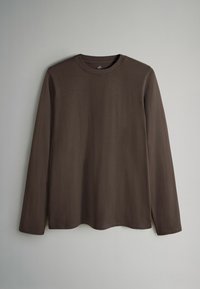 Cămașă maro cu mâneci lungi, realizată dintr-un material moale, cu guler rotund și tiv curbat. Fără modele sau detalii vizibile de accesorii.