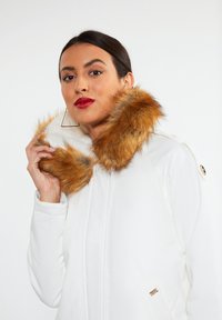 Hvid zip-jakke med en faux fur krave i brune og orange nuancer. Har sidelommer og hardware-detaljer i guld.