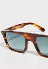 Lunettes de soleil rectangulaires en écaille de tortue avec des verres bleu foncé et le logo Ray-Ban dans le coin supérieur et à l'intérieur de la branche.