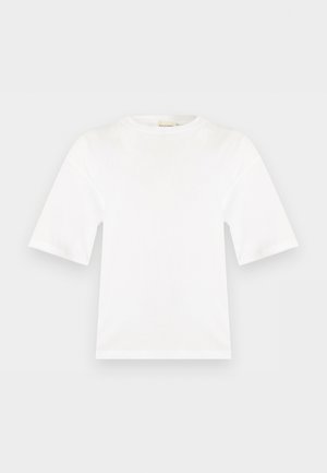 Άσπρη κοντομάνικη κοντή μπλούζα με στρογγυλή λαιμόκοψη, ίσια γραμμή και λεία υφή υφάσματος, εμφανίζεται σε μια επίπεδη ανοιχτόγριζη επιφάνεια.