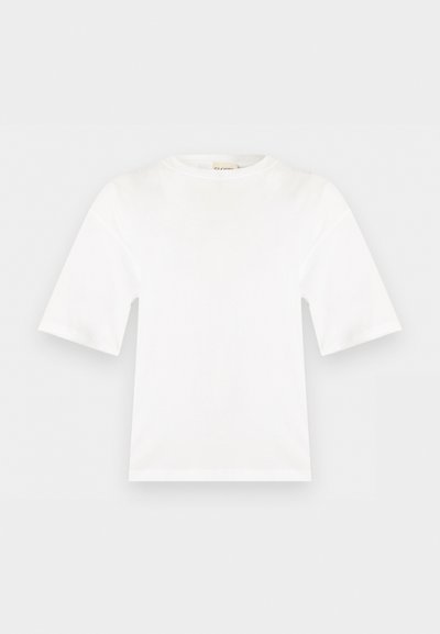 Άσπρη κοντομάνικη κοντή μπλούζα με στρογγυλή λαιμόκοψη, ίσια γραμμή και λεία υφή υφάσματος, εμφανίζεται σε μια επίπεδη ανοιχτόγριζη επιφάνεια.