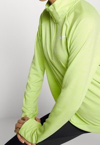 Langarm-Halbzip-Pullover in leuchtendem Limettengrün, aus leichtem, strukturiertem Stoff mit einem kleinen weißen Logo auf der Brust.