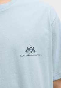Lyseblå bomulds t-shirt med korte ærmer, rund halsudskæring og et trykt design af to heste med "CONTEMPORARY CONCEPTS" nedenfor.