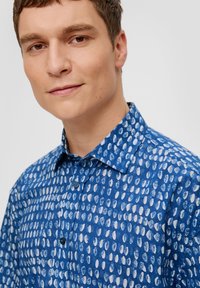 Modra srajca z gumbi, ki ima vzorec belih ovalnih oblik, izdelana iz teksturirane tkanine z ovratnikom in enim gumbom za zapiranje.