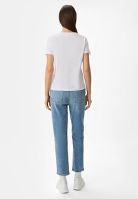 Camiseta de algodón blanca con mangas cortas y escote redondo, combinada con jeans de pierna recta en azul claro, con corte recto y bolsillos clásicos.
