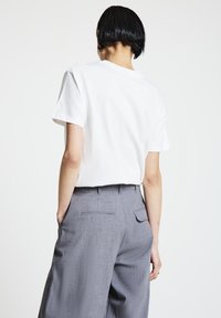T-shirt blanc en coton à manches courtes, associé à un pantalon gris à jambes larges avec une texture subtile et des poches arrière.