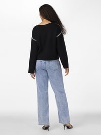 Black knit sweater featuring white stitching along the shoulders, paired with light blue straight-leg jeans. The model is seen from the back.