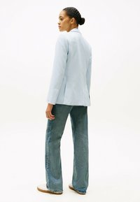 Blazer su misura di un blu chiaro con una texture morbida, abbinato a jeans svasati di un blu sbiadito. Sneakers bianche completano il look.