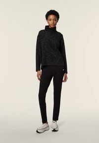 Maglietta nera a maniche lunghe con stampa leopardata sottile e collo alto, abbinata a pantaloni neri e sneakers bianche con dettagli neri.