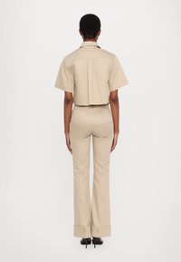 Cropped beige short-sleeve shirt and matching fitted trousers with flared cuffs. Smooth fabric texture, minimalist design with clean lines.