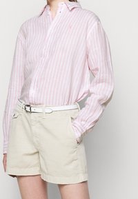 Rosa och vita randiga skjortknappen i kombination med beige shorts. Skjortan har klassisk krage och långa ärmar; shortsen har sidofickor.