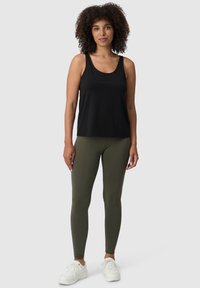 Top nero senza maniche con scollatura rotonda, abbinato a leggings verde oliva e scarpe da ginnastica bianche, su uno sfondo neutro.
