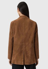 Bruine suède blazer met een rechte snit, lange mouwen en een rugventilatie. De gladde textuur en minimale stikdetails versterken het ontwerp.