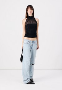 Schwarzes ärmelloses Top mit transparenten Details und gerafftem Halsausschnitt; kombiniert mit hellblauen, weiten Jeans und schwarzen spitzen Ballerinas. Ein einfaches Accessoire ist enthalten.