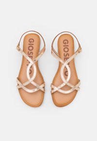 Sandales métalliques dorées à brides croisées avec une semelle plate et une semelle intérieure beige. Elle dispose d'une fermeture à boucle et d'une texture lisse.
