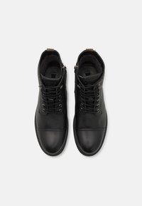 Botas de cuero negras hasta el tobillo con cordones, puntera redonda y suelas planas. Presentan una parte superior texturizada y un pequeño logo en la lengua.
