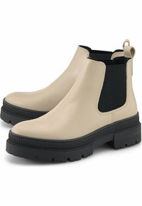Béžové Chelsea boty s černými elastickými panely, kulatou špičkou a masivními černými gumovými podrážkami. Hladká kožená textura s poutky na obouvání.