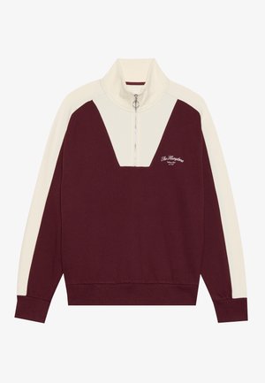 El sudadera de cuello con cremallera en burdeos y crema presenta un diseño de chevron, puños acanalados y un sutil logo en el pecho. Textura de tela suave.