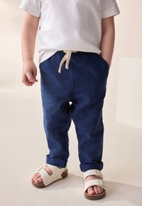 Marineblå linnedbukser med snøre i taljen, opbukne manchetter og to sidelommer, kombineret med hvide sandaler med korksål.