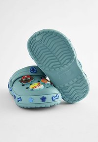 Saboturi bleu deschis cu figuri de câine din desene animate și accente în formă de os, având orificii ventilate și o talpă texturată pentru aderență.