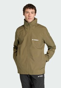 Olive green waterproof jacket with high collar, front zipper, and logo on the left chest. Textured fabric with long sleeves.