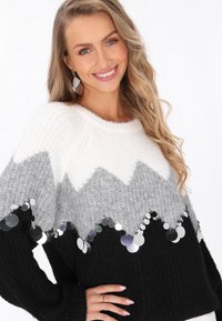 Fekete, szürke és fehér kötött pulóver cikk-cakk mintával, kör alakú flitterekkel díszítve az alsó szegély mentén. Puha tapintású, széles ujjak.